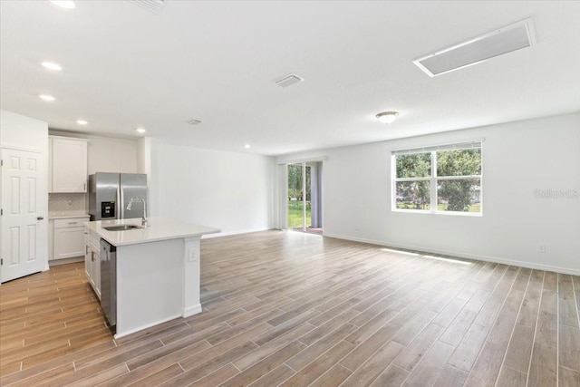 kitchen with backsplash, a kitchen island with sink, light hardwood / wood-style flooring, white cabinetry, and stainless steel appliances