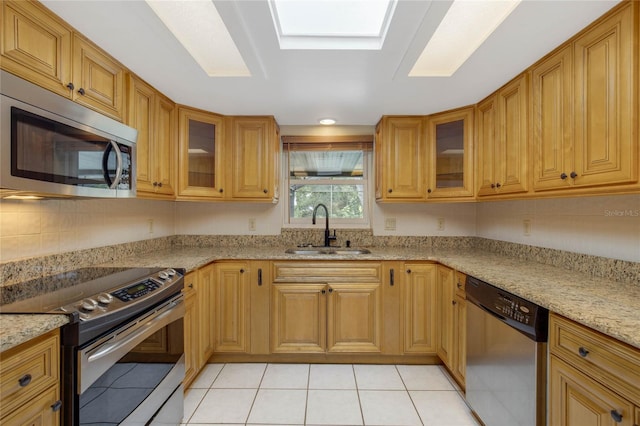 kitchen featuring sink, a skylight, light tile patterned floors, light stone counters, and stainless steel appliances