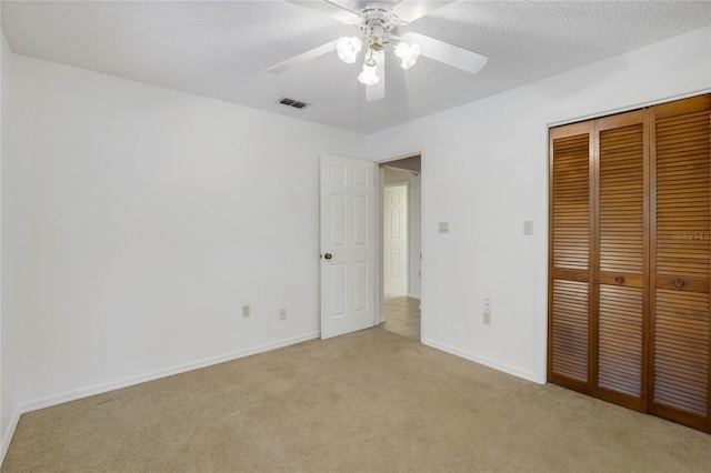 unfurnished bedroom with a textured ceiling, ceiling fan, light carpet, and a closet