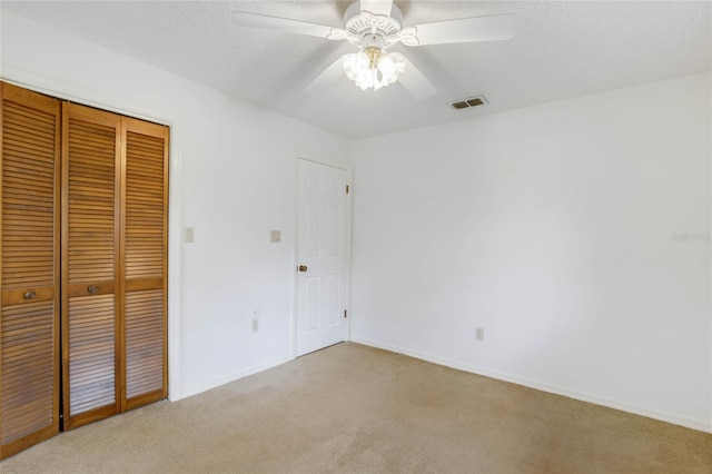 unfurnished bedroom featuring a textured ceiling, ceiling fan, light carpet, and a closet