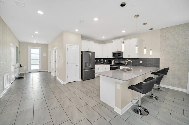 kitchen featuring kitchen peninsula, white cabinets, hanging light fixtures, a breakfast bar, and stainless steel appliances