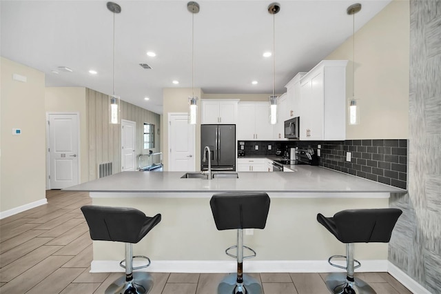 kitchen featuring kitchen peninsula, hanging light fixtures, a breakfast bar area, appliances with stainless steel finishes, and white cabinetry