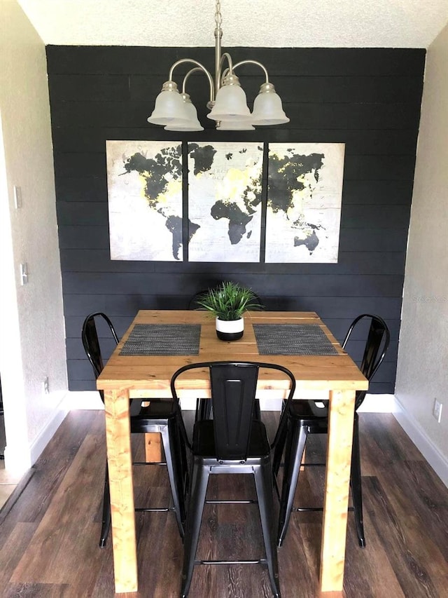 dining area with a textured ceiling, wooden walls, dark hardwood / wood-style floors, and a notable chandelier