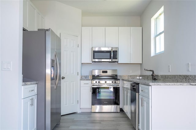 kitchen featuring white cabinetry, light stone counters, stainless steel appliances, and wood-type flooring