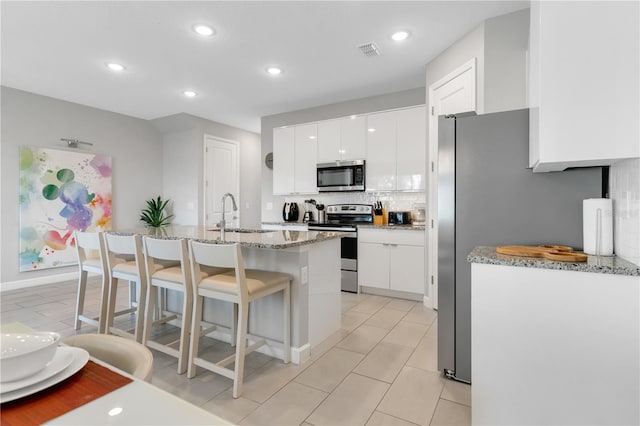 kitchen with sink, a kitchen bar, a kitchen island with sink, white cabinets, and appliances with stainless steel finishes