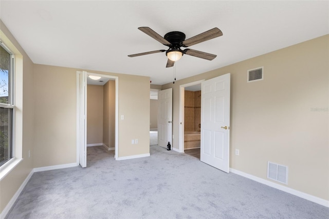 unfurnished bedroom featuring a closet, a spacious closet, light colored carpet, ensuite bathroom, and ceiling fan