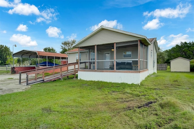 rear view of property with a sunroom, a lawn, a carport, and a storage shed