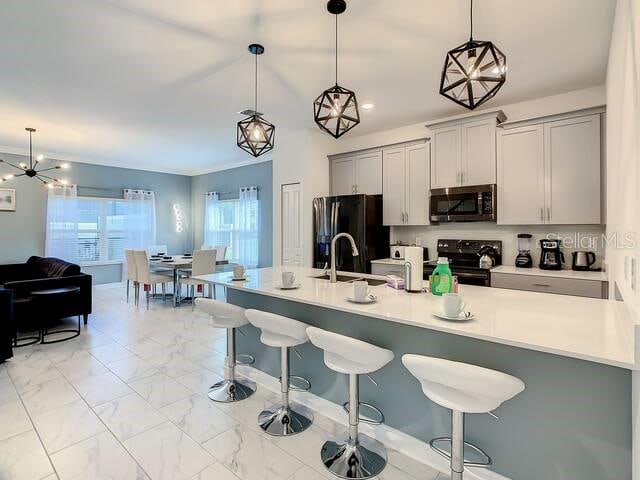 kitchen featuring gray cabinets, appliances with stainless steel finishes, a kitchen bar, and pendant lighting