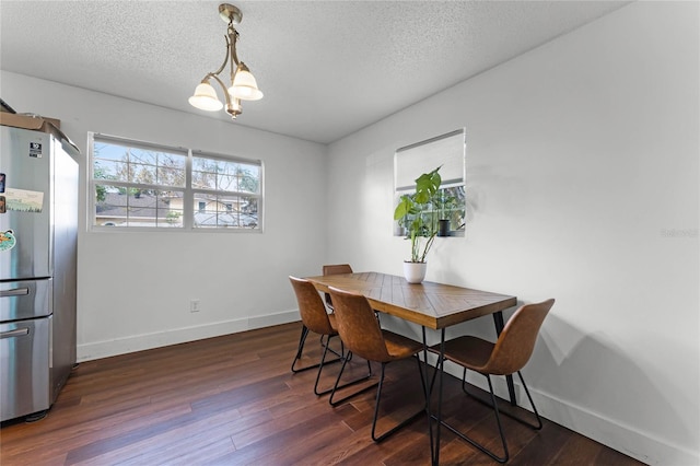 dining space featuring dark wood-type flooring, a textured ceiling, and an inviting chandelier