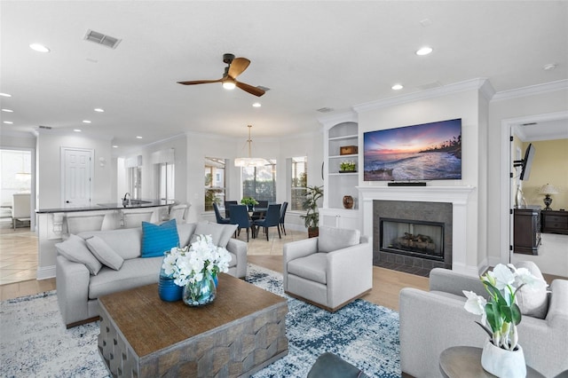 tiled living room featuring a tile fireplace, crown molding, and ceiling fan with notable chandelier