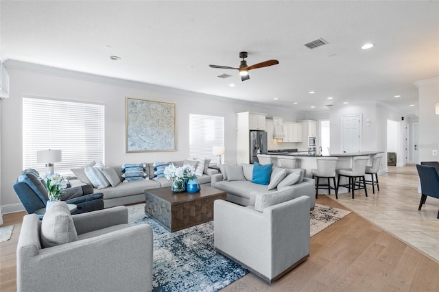 living room with ornamental molding, light wood-type flooring, and ceiling fan