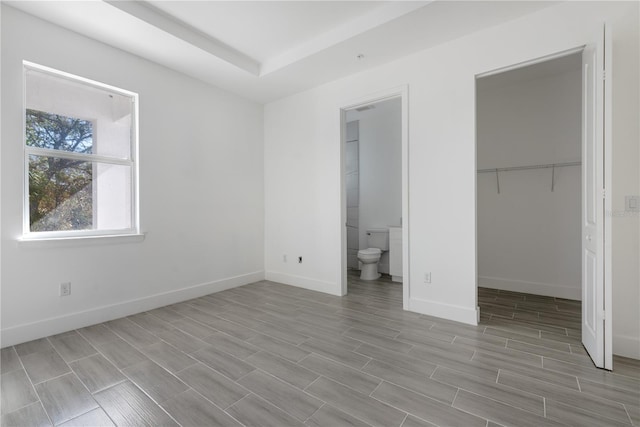 unfurnished bedroom with a closet, a spacious closet, light hardwood / wood-style floors, and ensuite bathroom