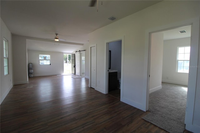 empty room featuring a barn door, dark hardwood / wood-style floors, and ceiling fan