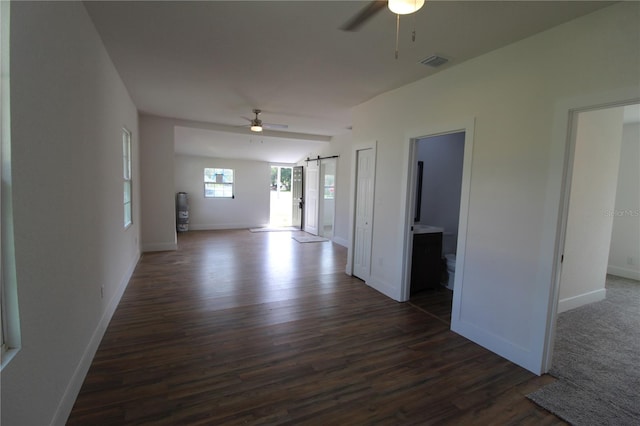 spare room featuring a barn door, dark wood-type flooring, and ceiling fan