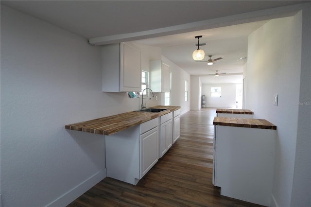 kitchen with white cabinets, hanging light fixtures, wood counters, dark wood-type flooring, and sink