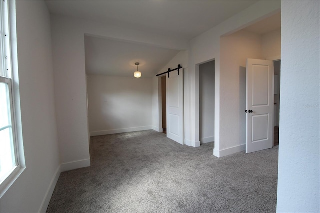 empty room with a barn door, carpet flooring, and vaulted ceiling