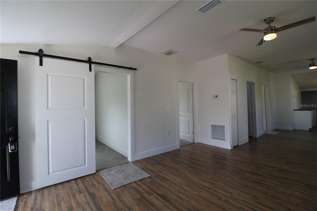 interior space with ceiling fan, dark hardwood / wood-style floors, vaulted ceiling, and a barn door