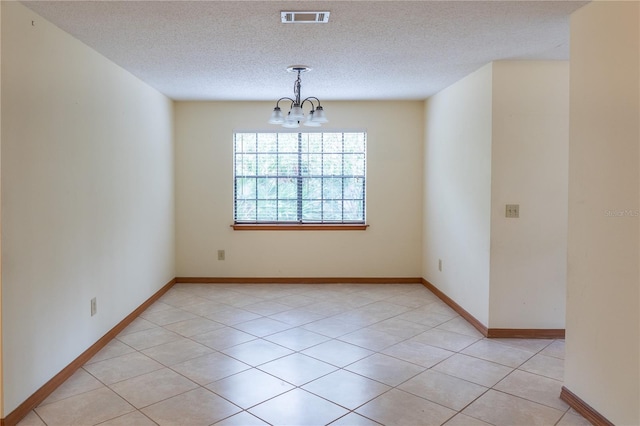 tiled spare room featuring a textured ceiling and a chandelier