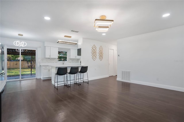 kitchen with white cabinetry, tasteful backsplash, dark wood-type flooring, and a kitchen bar