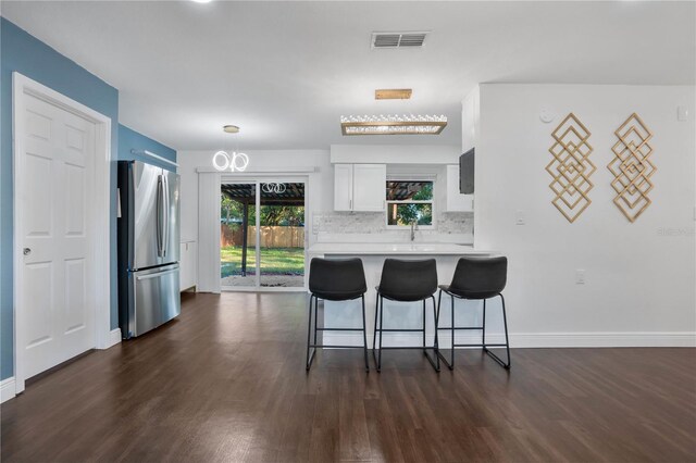 kitchen with kitchen peninsula, tasteful backsplash, dark hardwood / wood-style flooring, white cabinetry, and stainless steel refrigerator