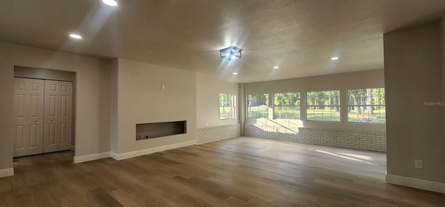 unfurnished living room featuring dark wood-type flooring, brick wall, and a textured ceiling