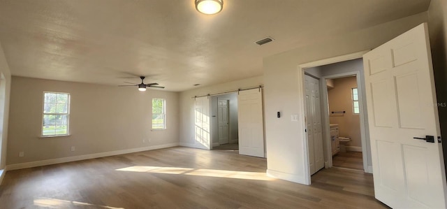 unfurnished bedroom with connected bathroom, ceiling fan, hardwood / wood-style floors, and a barn door