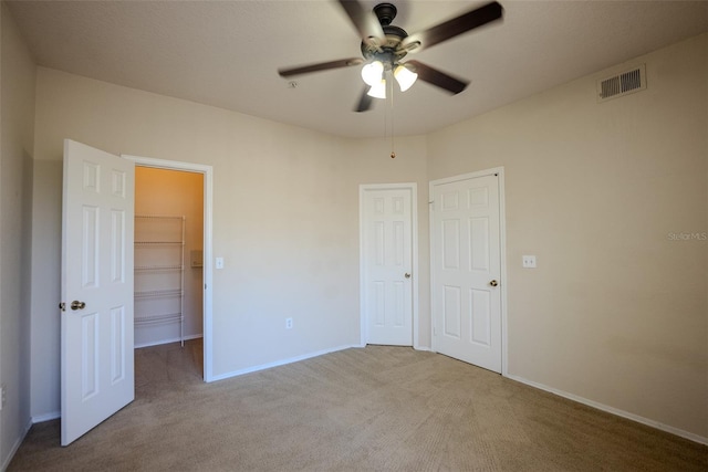 unfurnished bedroom featuring ceiling fan, a walk in closet, and light colored carpet