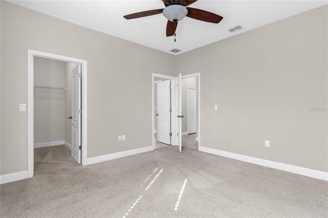 unfurnished bedroom with a spacious closet, light colored carpet, a closet, and ceiling fan