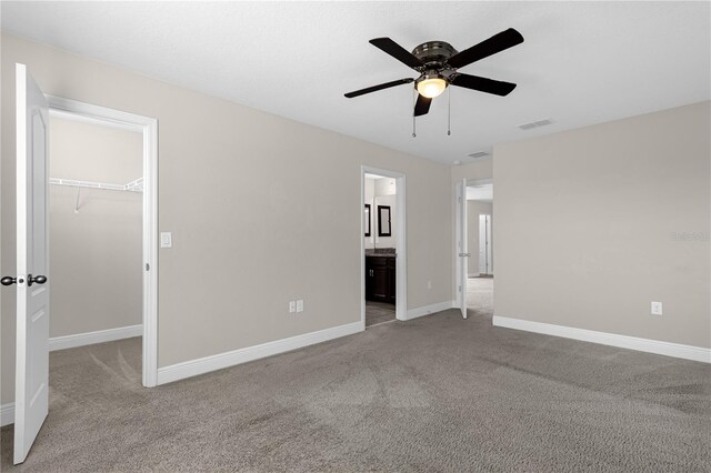 interior space with ceiling fan, connected bathroom, a closet, a walk in closet, and light colored carpet