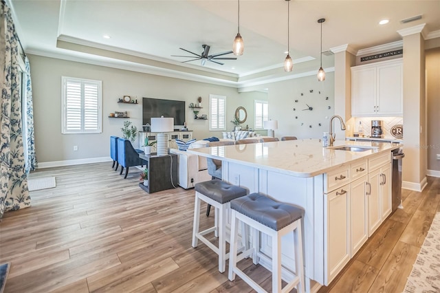 kitchen with a kitchen island with sink, decorative light fixtures, white cabinetry, light stone counters, and light hardwood / wood-style floors