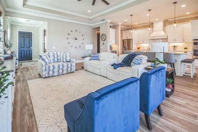 living room featuring ceiling fan, ornamental molding, sink, and light wood-type flooring