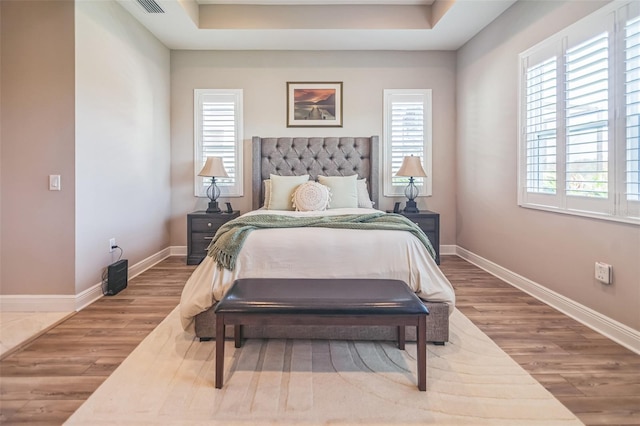 bedroom with a tray ceiling, wood-type flooring, and multiple windows