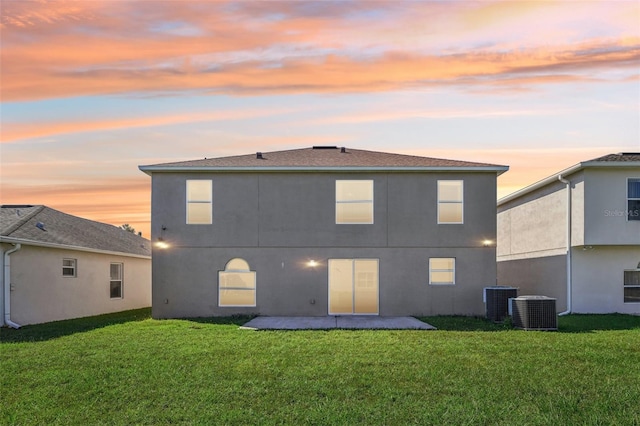 back house at dusk with a patio, central AC, and a lawn