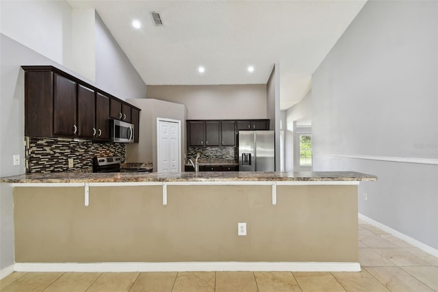 kitchen featuring kitchen peninsula, dark brown cabinetry, stainless steel appliances, and a breakfast bar area