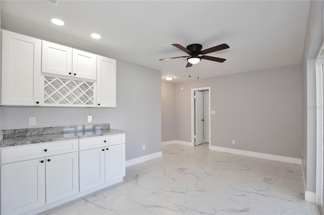 kitchen featuring ceiling fan, light stone counters, and white cabinets