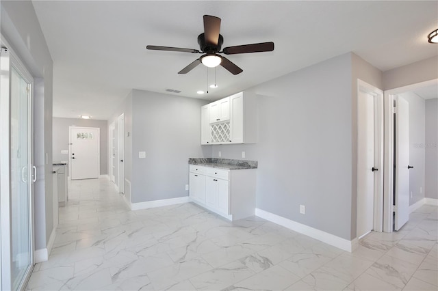 interior space with ceiling fan, light stone counters, and white cabinets