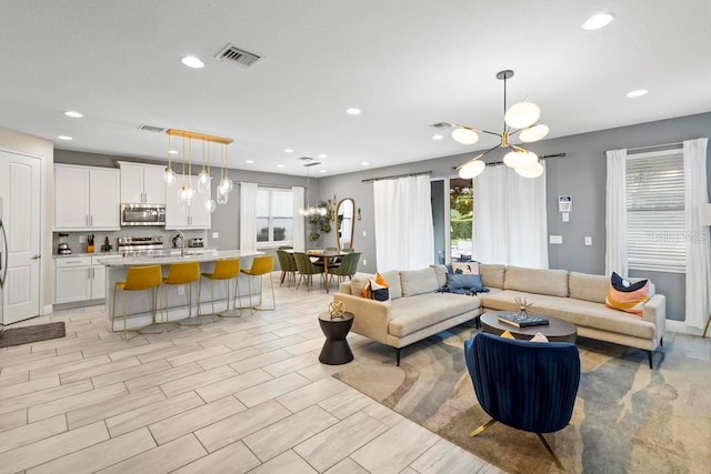 living room featuring light hardwood / wood-style flooring, a notable chandelier, sink, and plenty of natural light