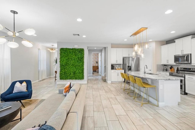 kitchen featuring white cabinets, an island with sink, appliances with stainless steel finishes, a breakfast bar, and sink