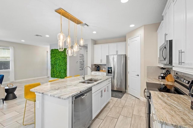 kitchen with appliances with stainless steel finishes, sink, pendant lighting, white cabinets, and a center island with sink