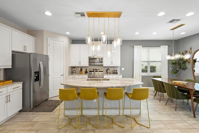 kitchen featuring stainless steel appliances, decorative light fixtures, and a kitchen island with sink