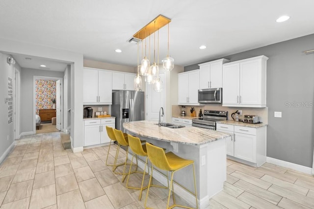 kitchen featuring appliances with stainless steel finishes, white cabinets, sink, and an island with sink