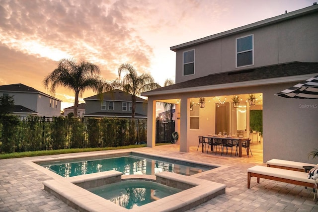 pool at dusk featuring an in ground hot tub and a patio area