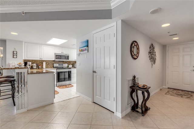 kitchen featuring a kitchen breakfast bar, stainless steel appliances, dark stone countertops, light tile patterned floors, and white cabinets