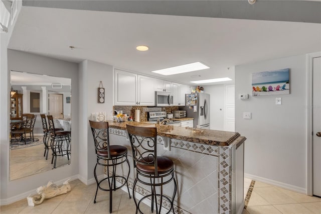 kitchen with a kitchen breakfast bar, kitchen peninsula, white cabinets, light tile patterned floors, and appliances with stainless steel finishes