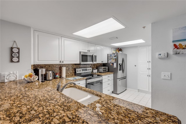 kitchen with kitchen peninsula, sink, white cabinets, light tile patterned floors, and appliances with stainless steel finishes