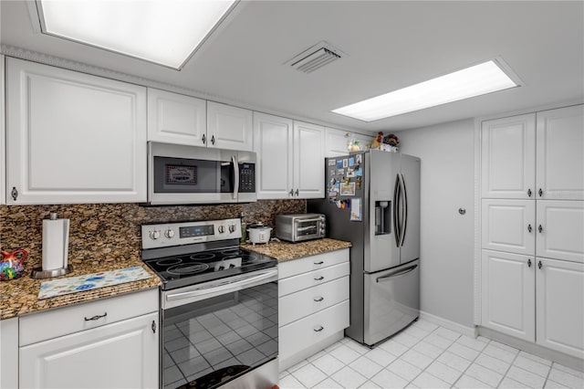 kitchen featuring appliances with stainless steel finishes, white cabinetry, dark stone counters, and light tile patterned floors