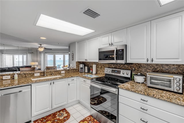 kitchen featuring sink, white cabinetry, stainless steel appliances, dark stone countertops, and light tile patterned floors