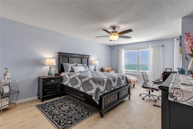 bedroom featuring a water view, a textured ceiling, light wood-type flooring, and ceiling fan