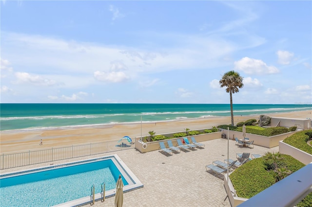 view of pool featuring a patio, a water view, and a beach view