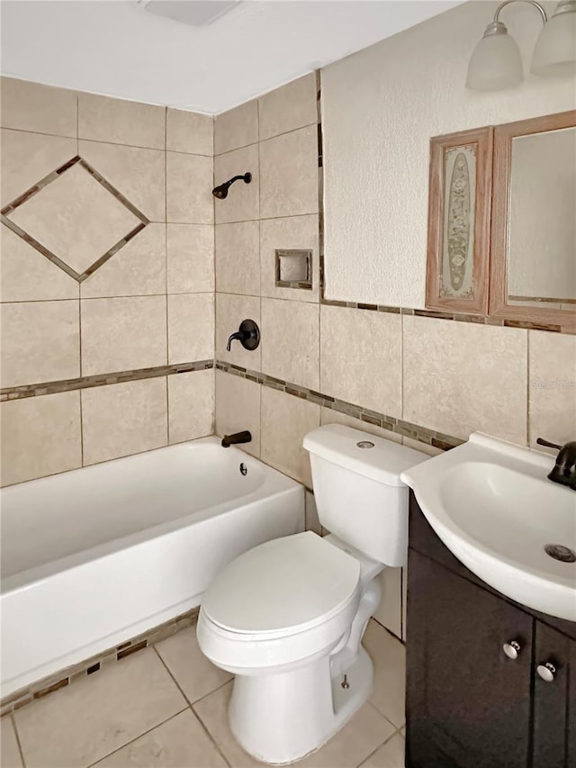 full bathroom featuring toilet, tile patterned flooring, tiled shower / bath, vanity, and tile walls